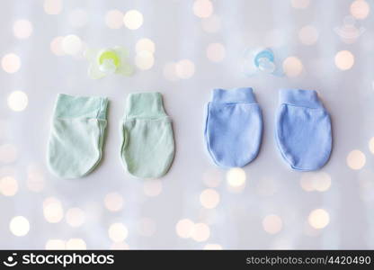 clothing, babyhood, accessory and object concept - close up of baby mittens and soothers for newborn twins with holidays lights