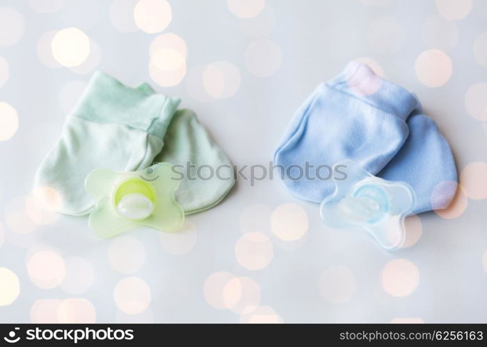 clothing, babyhood, accessory and object concept - close up of baby mittens and soothers for newborn twins