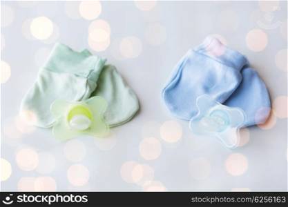 clothing, babyhood, accessory and object concept - close up of baby mittens and soothers for newborn twins
