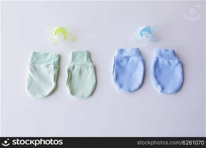clothing, babyhood, accessory and object concept - close up of baby mittens and soothers for newborn twins