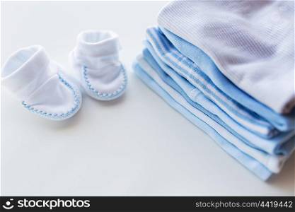 clothing, babyhood, motherhood and object concept - close up of baby bootees on pile of folded clothes for newborn boy