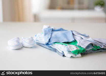 clothing, babyhood, motherhood and object concept - close up of baby bootees and pile of clothes for newborn boy at home