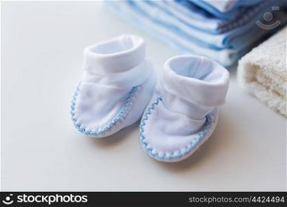 clothing, babyhood, motherhood and object concept - close up of baby bootees and pile of clothes for newborn boy