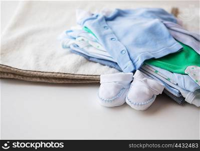 clothing, babyhood, motherhood and object concept - close up of baby bootees and pile of clothes for newborn boy