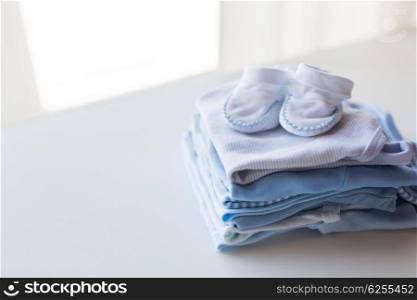 clothing, babyhood, motherhood and object concept - close up of baby bootees on pile of folded clothes for newborn boy
