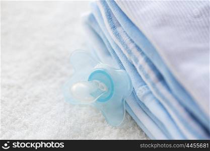 clothing, babyhood, motherhood and object concept - close up of baby soother and pile of clothes for newborn boy