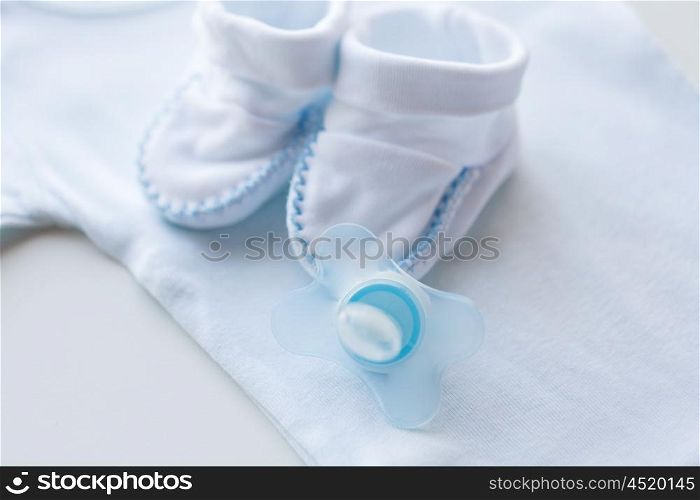 clothing, babyhood, motherhood and object concept - close up of baby soother, bootees and bodysuit for newborn boy