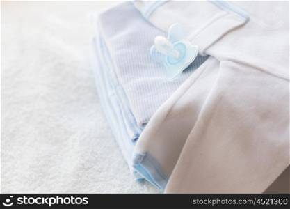clothing, babyhood, motherhood and object concept - close up of baby soother and pile of clothes for newborn boy