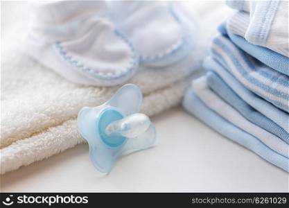clothing, babyhood, motherhood and object concept - close up of baby soother, bootees and pile of clothes for newborn boy