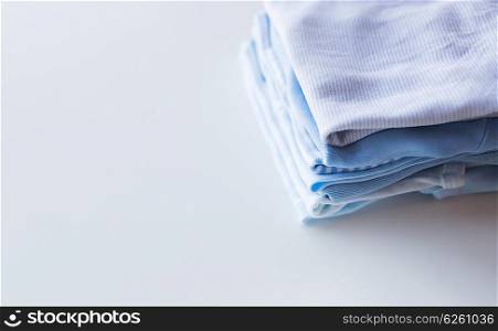 clothing, babyhood, motherhood and object concept - close up of pile of baby clothes for newborn boy folded on table