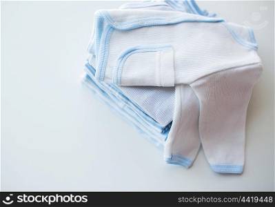 clothing, babyhood, motherhood and object concept - close up of white baby cardigan with pile of folded clothes for newborn boy