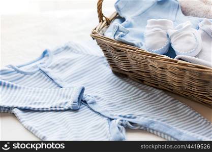 clothing, babyhood, motherhood and object concept - close up of white baby bootees with pile of clothes and towel for newborn boy in basket on table