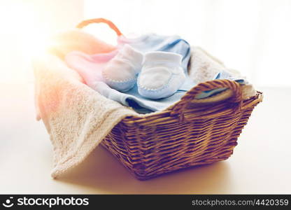 clothing, babyhood, motherhood and object concept - close up of white baby bootees with pile of clothes and towel for newborn boy in basket on table