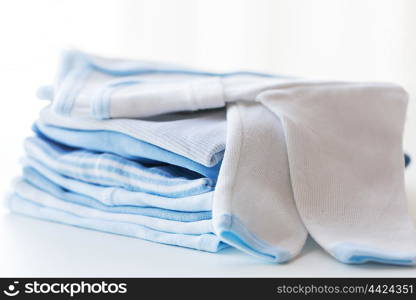 clothing, babyhood, motherhood and object concept - close up of white baby cardigan with pile of folded clothes for newborn boy