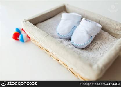 clothing, babyhood, motherhood and object concept - close up of white baby bootees for newborn boy on towel in basket