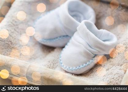 clothing, babyhood, motherhood and object concept - close up of white baby bootees for newborn boy on towel in basket