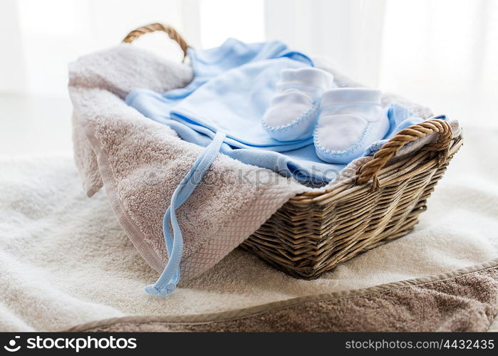 clothing, babyhood, motherhood and object concept - close up of white baby bootees with pile of clothes and towel for newborn boy in basket on table