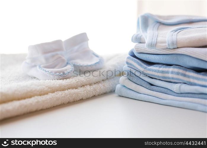 clothing, babyhood, motherhood and object concept - close up of white baby bootees, towel and pile of clothes for newborn boy