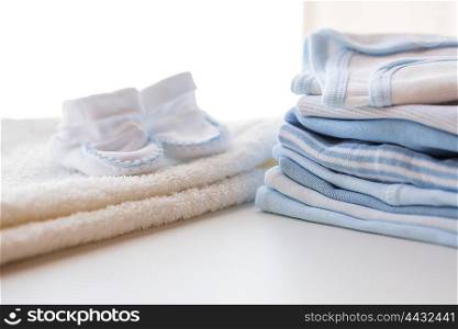 clothing, babyhood, motherhood and object concept - close up of white baby bootees, towel and pile of clothes for newborn boy