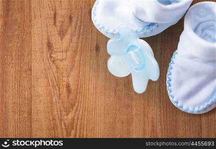 clothing, babyhood, motherhood and object concept - close up of white baby bootees and soother for newborn boy on wooden background