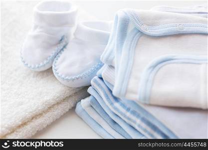 clothing, babyhood, motherhood and object concept - close up of white baby bootees with pile of clothes for newborn boy