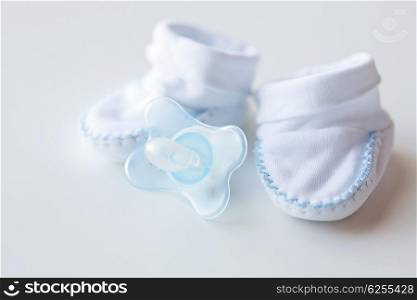 clothing, babyhood, motherhood and object concept - close up of white baby bootees and soother for newborn boy