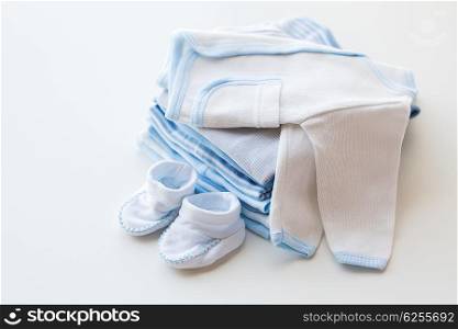 clothing, babyhood, motherhood and object concept - close up of white baby cardigan with bootees and pile of clothes for newborn boy