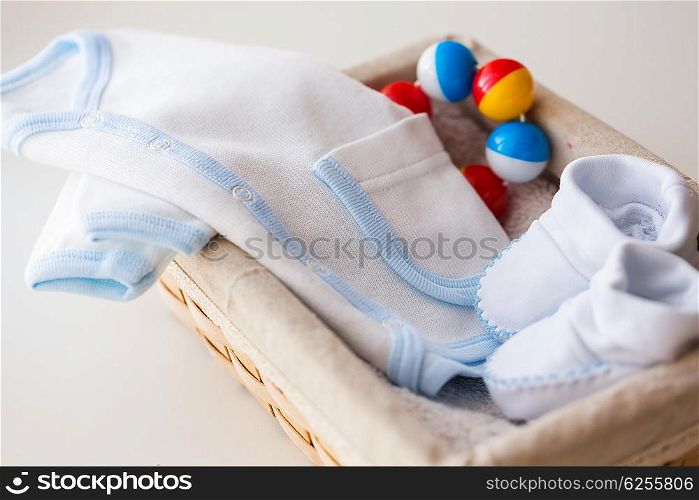 clothing, babyhood, motherhood and object concept - close up of white baby bootees with cardigan and rattle for newborn boy in basket on table