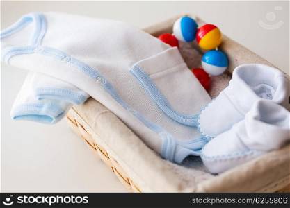 clothing, babyhood, motherhood and object concept - close up of white baby bootees with cardigan and rattle for newborn boy in basket on table