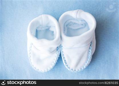 clothing, babyhood, motherhood and object concept - close up of white baby bootees for newborn boy on blue