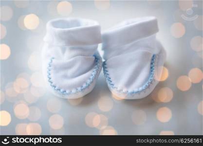 clothing, babyhood, motherhood and object concept - close up of white baby bootees for newborn boy