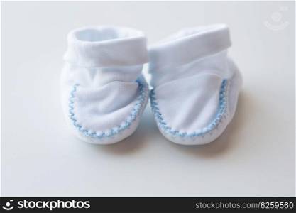 clothing, babyhood, motherhood and object concept - close up of white baby bootees for newborn boy