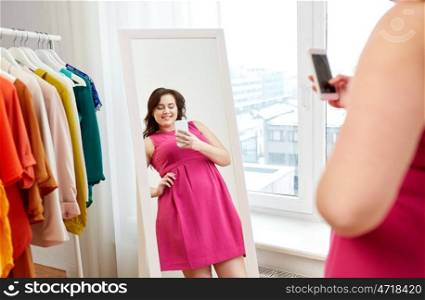 clothing, fashion and people concept - happy plus size woman in pink dress taking at mirror selfie by smartphone at home. plus size woman taking at mirror selfie at home. plus size woman taking at mirror selfie at home