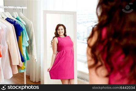 clothing, fashion and people concept - happy plus size woman in pink dress looking at mirror at home. happy plus size woman in dress looking at mirror