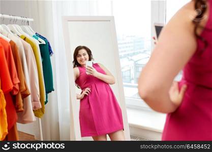 clothing, fashion and people concept - happy plus size woman in pink dress taking at mirror selfie by smartphone at home. plus size woman taking at mirror selfie at home