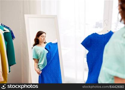 clothing fashion and people concept - pensive plus size woman with blue dress at mirror at home. pensive plus size woman with blue dress at mirror