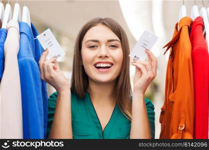 clothing, fashion, sale and people concept - happy woman showing price tags on clothes at shopping center or mall
