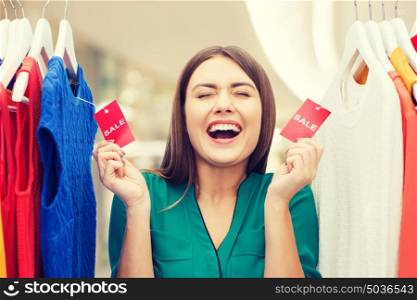 clothing, fashion, sale and people concept - happy woman showing tags on clothes at shopping center or mall. happy woman with sale tags on clothes at wardrobe
