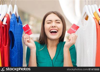 clothing, fashion, sale and people concept - happy woman showing tags on clothes at shopping center or mall