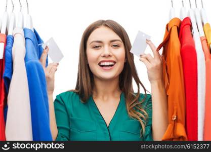 clothing, fashion, sale, shopping and people concept - happy woman showing blank tags on clothes at home wardrobe or shop
