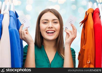clothing, fashion, sale, shopping and people concept - happy woman showing price tags on clothes at wardrobe over blue holidays lights background