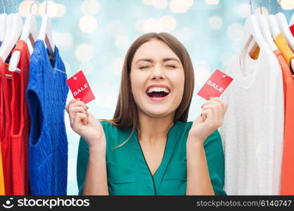 clothing, fashion, sale, shopping and people concept - happy woman showing tags on clothes at wardrobe over blue holidays lights background