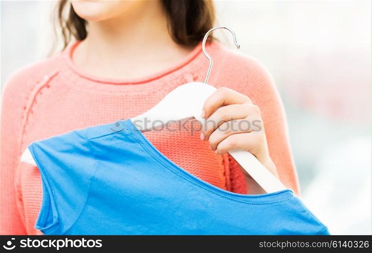 clothing, fashion, style and people concept - close up of happy young woman or teenage girl holding hanger with t-shirt