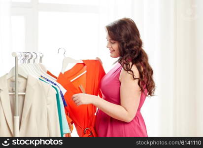 clothing, fashion, style and people concept - happy plus size woman choosing clothes at home wardrobe