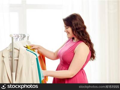 clothing, fashion, style and people concept - happy plus size woman choosing clothes at home wardrobe