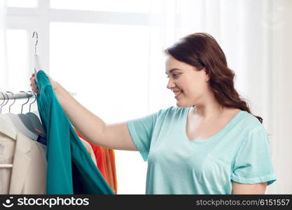 clothing, fashion, style and people concept - happy plus size woman choosing clothes at home wardrobe