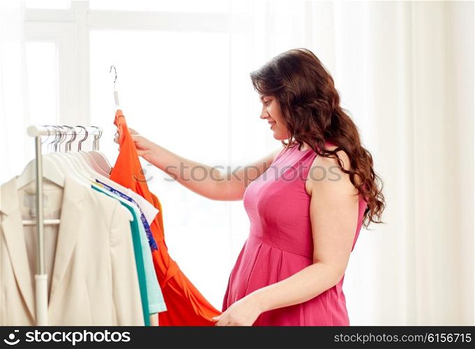 clothing, fashion, style and people concept - happy plus size woman choosing clothes at home wardrobe