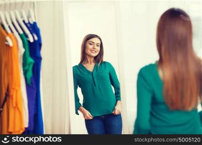 clothing, fashion, style and people concept - happy woman choosing clothes and posing at mirror at home wardrobe. happy woman posing at mirror in home wardrobe