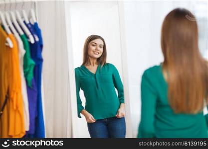 clothing, fashion, style and people concept - happy woman choosing clothes and posing at mirror at home wardrobe