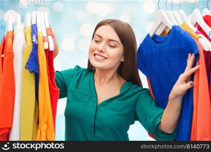 clothing, fashion, style and people concept - happy woman choosing clothes at wardrobe over blue holidays lights background